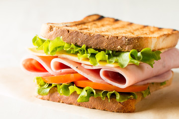 Close-up photo of a club sandwich. Sandwich with meat, prosciutto, salami, salad, vegetables, lettuce, tomato, onion and mustard on a fresh sliced rye bread on wooden background. Olives background.