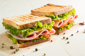 Close-up photo of a club sandwich. Sandwich with meat, prosciutto, salami, salad, vegetables, lettuce, tomato, onion and mustard on a fresh sliced rye bread on wooden background. Olives background.