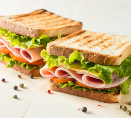 Close-up photo of a club sandwich. Sandwich with meat, prosciutto, salami, salad, vegetables, lettuce, tomato, onion and mustard on a fresh sliced rye bread on wooden background. Olives background.