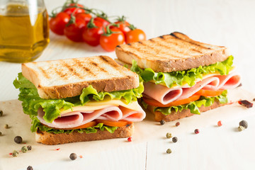 Close-up photo of a club sandwich. Sandwich with meat, prosciutto, salami, salad, vegetables, lettuce, tomato, onion and mustard on a fresh sliced rye bread on wooden background. Olives background.