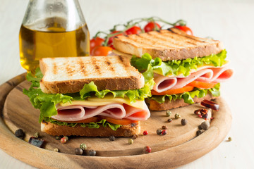Close-up photo of a club sandwich. Sandwich with meat, prosciutto, salami, salad, vegetables, lettuce, tomato, onion and mustard on a fresh sliced rye bread on wooden background. Olives background.