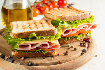 Close-up photo of a club sandwich. Sandwich with meat, prosciutto, salami, salad, vegetables, lettuce, tomato, onion and mustard on a fresh sliced rye bread on wooden background. Olives background.