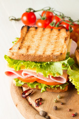 Close-up photo of a club sandwich. Sandwich with meat, prosciutto, salami, salad, vegetables, lettuce, tomato, onion and mustard on a fresh sliced rye bread on wooden background. Olives background.