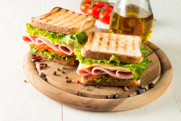 Close-up photo of a club sandwich. Sandwich with meat, prosciutto, salami, salad, vegetables, lettuce, tomato, onion and mustard on a fresh sliced rye bread on wooden background. Olives background.