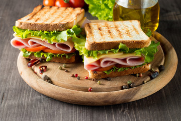 Close-up photo of a club sandwich. Sandwich with meat, prosciutto, salami, salad, vegetables, lettuce, tomato, onion and mustard on a fresh sliced rye bread on wooden background. Olives background.