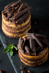 Chocolate cakes on black slatter board with mint, coffee beans on dark background, closeup photo. Fresh, tasty dessert food concept. 