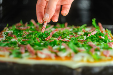 Process of making pizza. Italian pepperoni pizza with mushrooms, ruccola, tomatoes, mozzarella, garlic and sauce. Chef adds ingredients to pizza