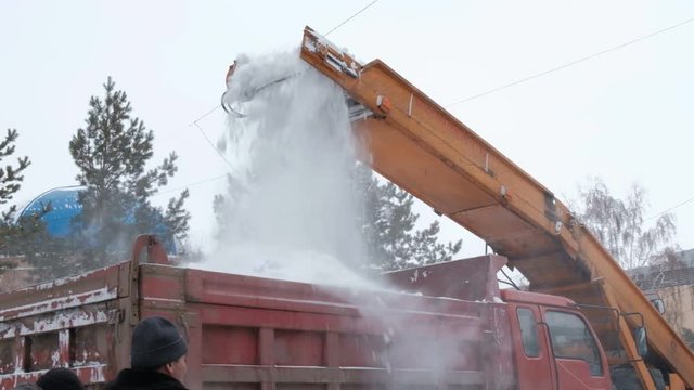Snow removal on the streets. Close-up of falling snowballs from a snowplow and into a truck body. Municipal urban road maintenance. Abundance of snow. Winter.