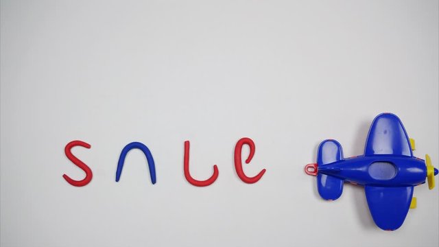 Blue toy plane moves on a white background. The trace of the turbines formed the word sale. Stop motion