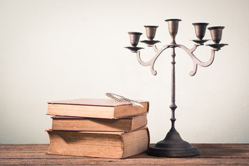 still photography : stack of old book with feather pen and candelabrum on old wooden table with space of blank wall