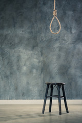 The old chair with the noose hanging at above with concrete wall at back, failure or commit suicide...