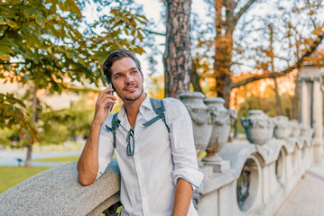 Young man holding mobile phone, using smartphone, making a call, talking on the phone, standing on sunny street