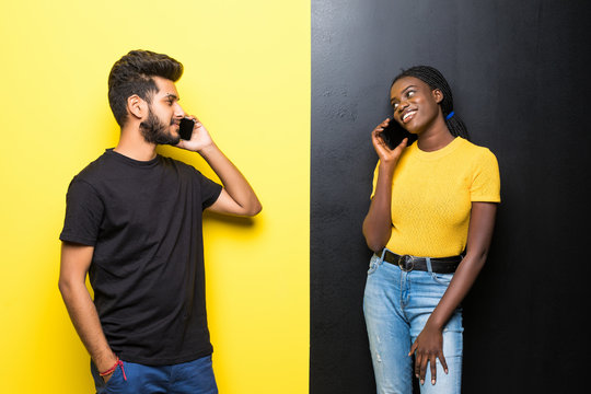 Young happy mixed race couple, indian man and african woman talking on the phone isolated on different yellow and black background