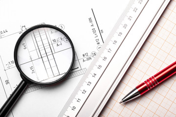 Silver ruler, red pen and magnifying glass on white paper with project lines. Top view engineering background. 