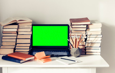 Green screen laptop, stack of books, notebooks and pencils on white table, education office concept background.