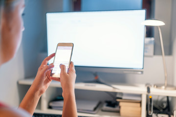Woman hand working and smart phone and laptop on wooden desk in office in morning light.