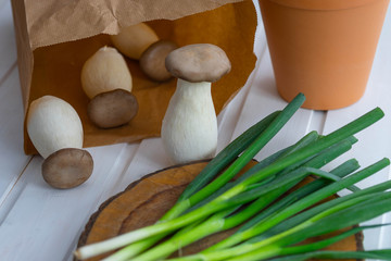 king oyster mushrooms in an environmentally friendly brown paper bag, green onions on a wooden board 