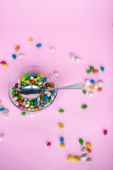 colorful candy in clear wrappers piled in a glass vase isolated on pink background