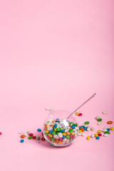 colorful candy in clear wrappers piled in a glass vase isolated on pink background