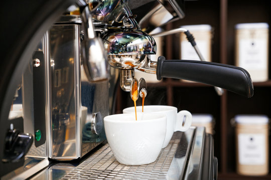 Coffee brewing in coffee machine. Espresso pouring in two white cups. Shallow focus, dark blurred background.