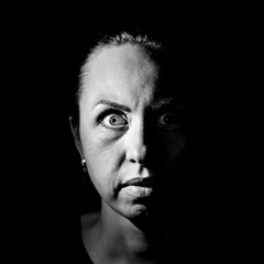 Portrait of a scared or surprised caucasian woman. Scary and fear concept. Black and white shot, low key lighting. Isolated on black.