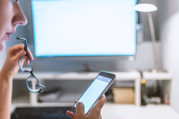 Successful business woman looking at mobile cell phone while at home in office work space