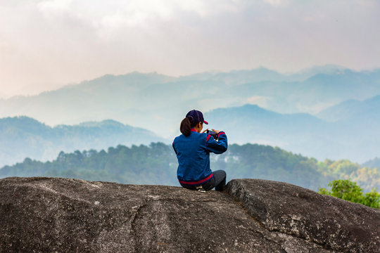 Girl makes landscape photo with help of smartphone. Landscape contains sundown over mountains.