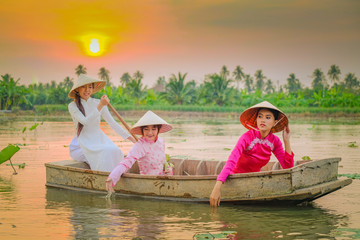 Fototapeta na wymiar Three Vietnamese girls are rowing in the lotus garden at sunset.