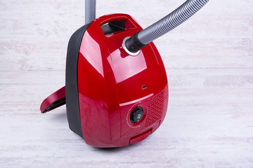 Red vacuum cleaner on white wooden background.