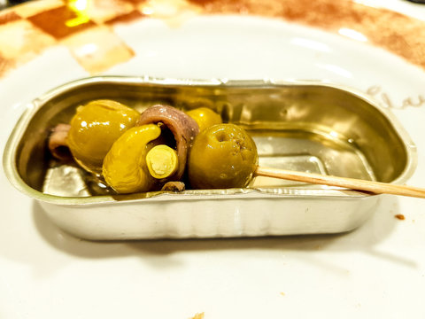 Canapes of green olives and chilli wrapped in Cantabrian anchovy presented in the metal tray of the olives.