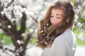 Closeup beauty portrait of young attractive woman outdoor on spring background. Smiling girl with flowers in her blond hair. Curly hair female.