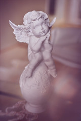 plaster angel figurine on pink background. Cute little angel statue thinking. Soft focus, watercolor pink toning.