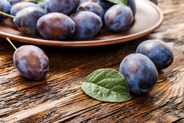Ripe plums in plate on a dark brown wooden table.