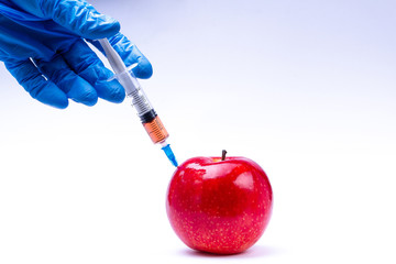 Pesticides and nitrates are injected into a red apple with a syringe. Gmo concept and genetically modified organism. Gmo free and natural fruits without chemical additives. - obrazy, fototapety, plakaty