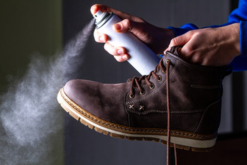 A person is cleaning and spraying agent on men's suede casual boots for protection from moisture...