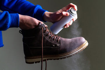 A person is cleaning and spraying agent on men's suede casual boots for protection from moisture and dirt. Shoe shine and care 