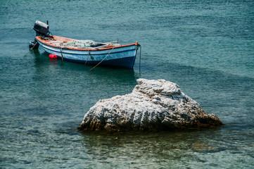 Fishing boat anchored in calm blue sea waters near sea rock in sunny summer day