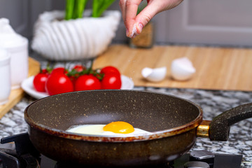 Fried homemade, chicken eggs in the frying pan sprinkling with spices for a healthy, protein breakfast