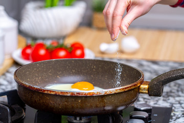 Fried homemade, chicken eggs in the frying pan sprinkling with spices for a healthy, protein breakfast