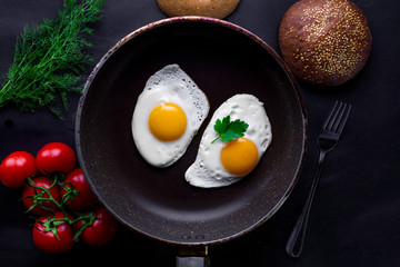 Homemade, fresh, fried eggs in a frying pan with dill, parsley, tomatoes and sesame bun for a healthy breakfast. Top view. Protein food