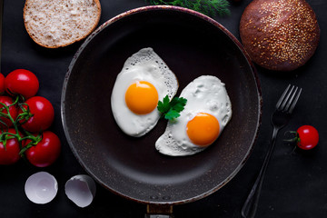 Fried eggs in a frying pan with dill, parsley, tomatoes cherry and sesame bun for a healthy breakfast. Top view. Protein food