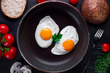 Homemade, fried chicken eggs in a frying pan with dill, parsley, tomatoes cherry and sesame bun for a healthy breakfast. Top view. Protein food