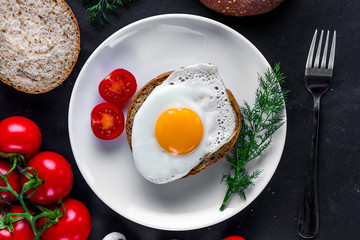 Fried chicken egg on a plate with dill, tomatoes cherry and sesame bun for a healthy breakfast. Protein food. Eggs sandwiches. Top view