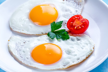 Homemade, fried chicken eggs with fresh parsley and cherry tomato close up on a plate for a healthy breakfast. Protein food.