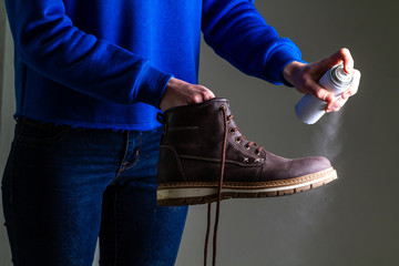 A person is cleaning and spraying agent on men's suede casual boots for protection from moisture and dirt. Shoe shine