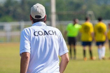 Back view of male football coach in white COACH shirt at an outdoor sport field