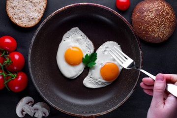 Homemade, fresh, fried eggs in a frying pan with dill, parsley, tomatoes and sesame bun for a healthy breakfast. Top view. Protein food