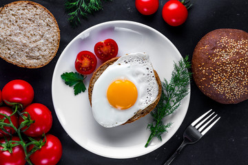 Homemade, fried chicken egg on a plate with dill, parsley, tomatoes cherry and sesame bun for a healthy breakfast. Protein food. Eggs sandwiches. Top view