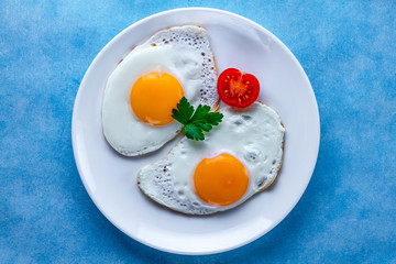 Homemade fried chicken eggs with fresh parsley and сherry tomato on a plate for a healthy breakfast. Protein food. Top view