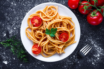 Delicious spaghetti with parsley, dill, tomatoes cherry and tomato sauce on a plate. Italian food and pasta. Top view